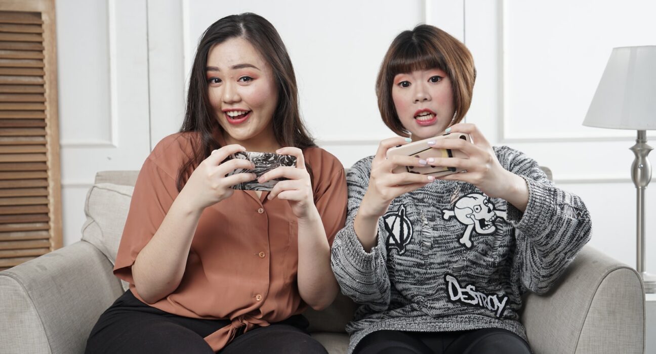 two women holding controllers sitting on sofa chair